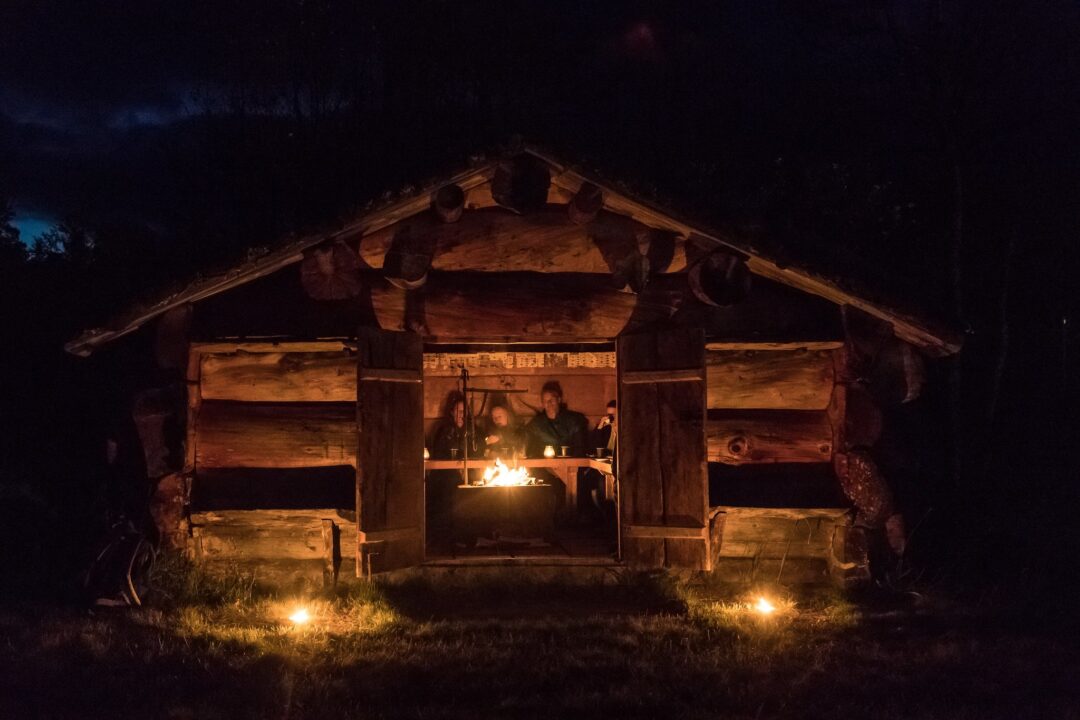 People gathered around a campfire in a wooden outdoor lodge at night in Sweden
