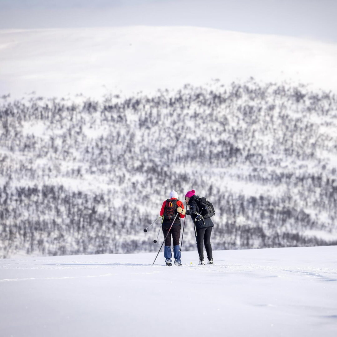 Two women cross-country skiing on a snowy slope with ski poles, outdoors in winter