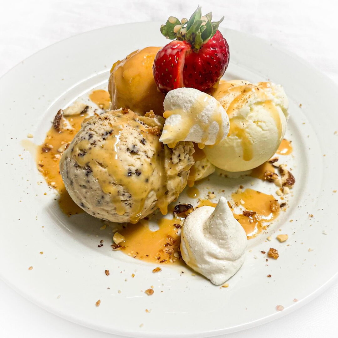 Dessert with scoops of ice cream, caramel sauce, strawberries and nuts on a white plate