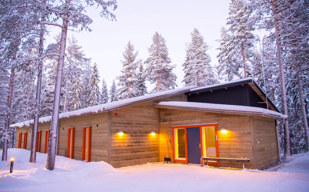 Snowy wooden cabin in a forest at dusk, Sweden Lapland winter lodge exterior