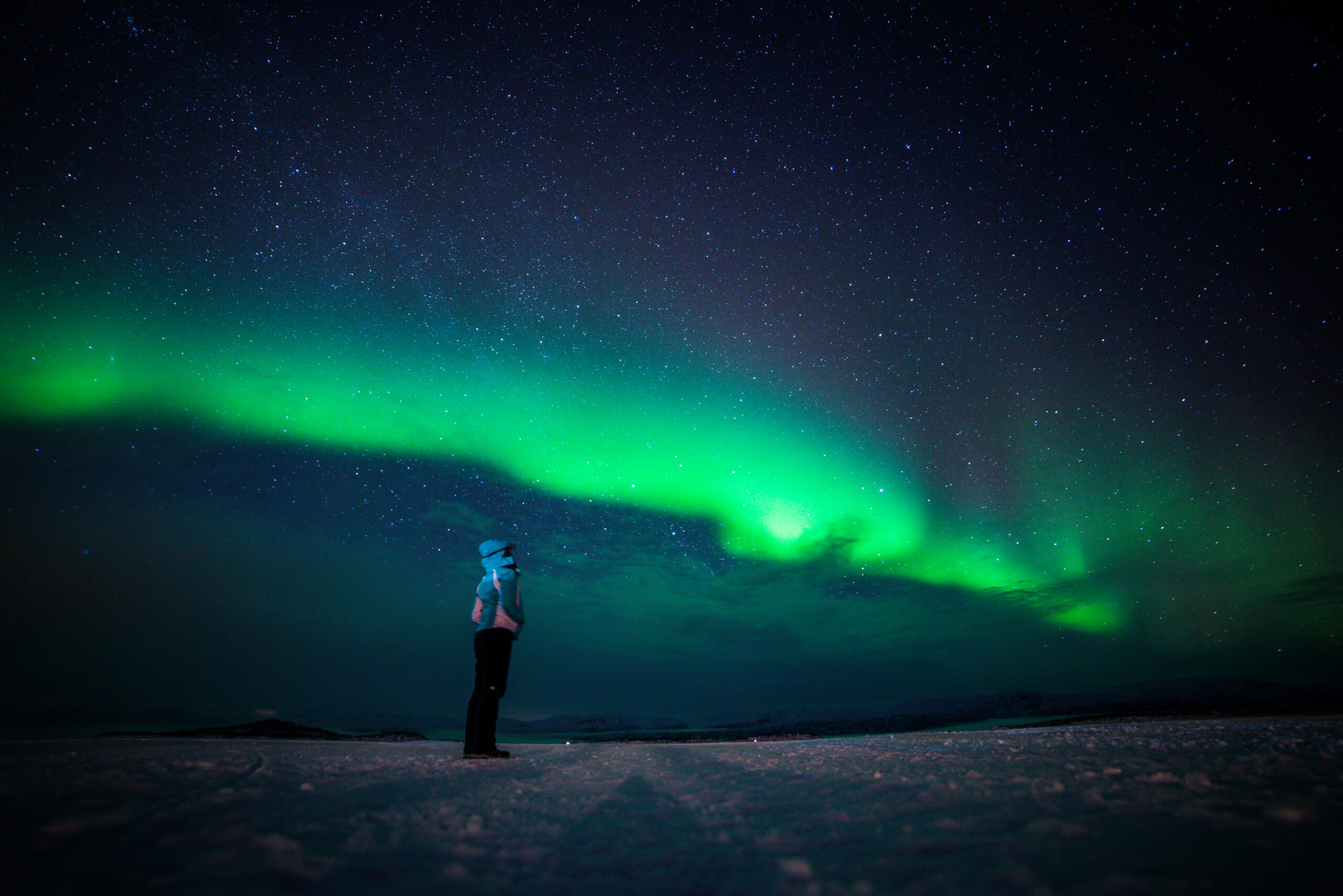 Woman standing on snow under green aurora borealis at night