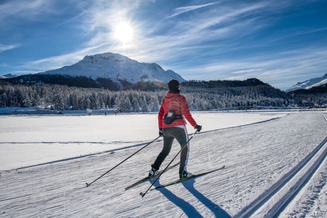 Woman cross-country skiing on snowy track with mountain peaks in the background.