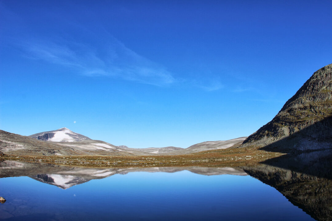 Mountain lake reflecting snow-capped peaks in a Norwegian national park valley, calm clear waters