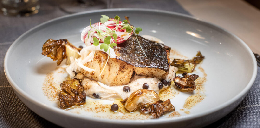 Swedish-style roast fish with potatoes, pickled radish and capers on a white plate in a dining setting
