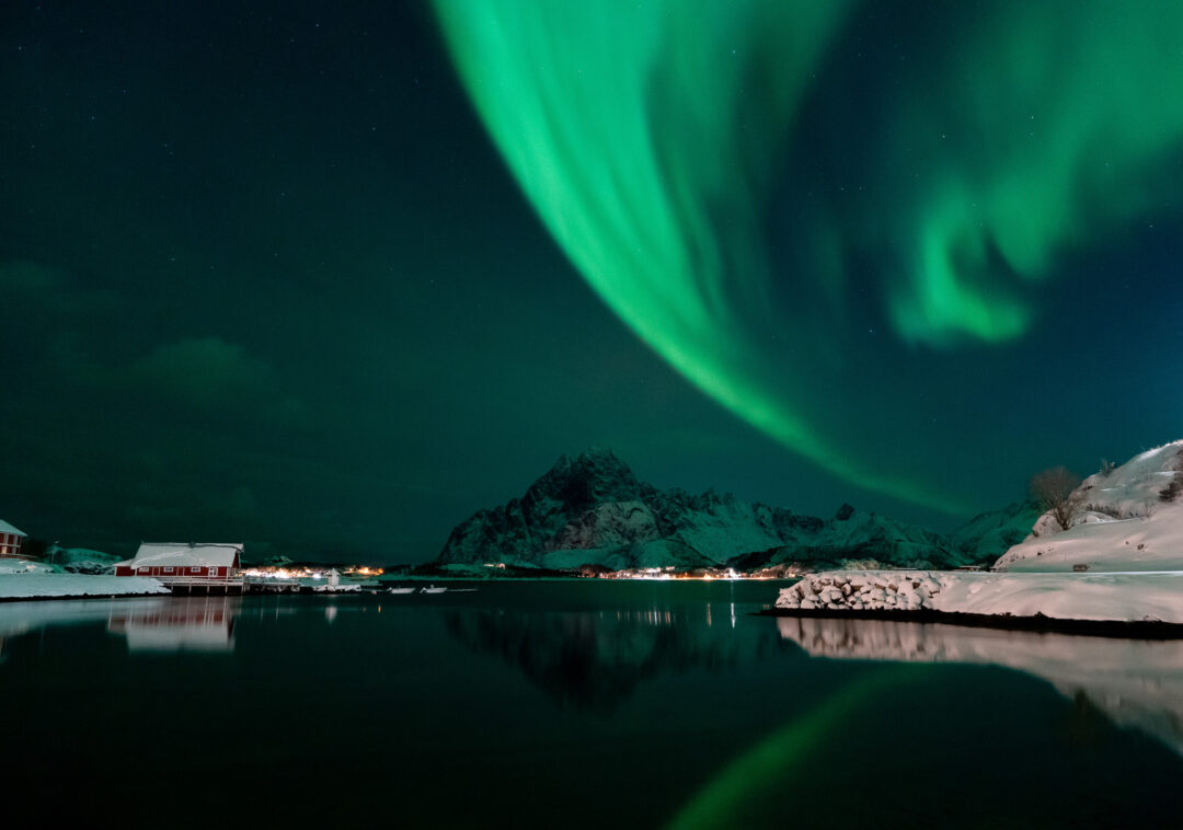 Northern lights over a snowy Lofoten village by the water at night