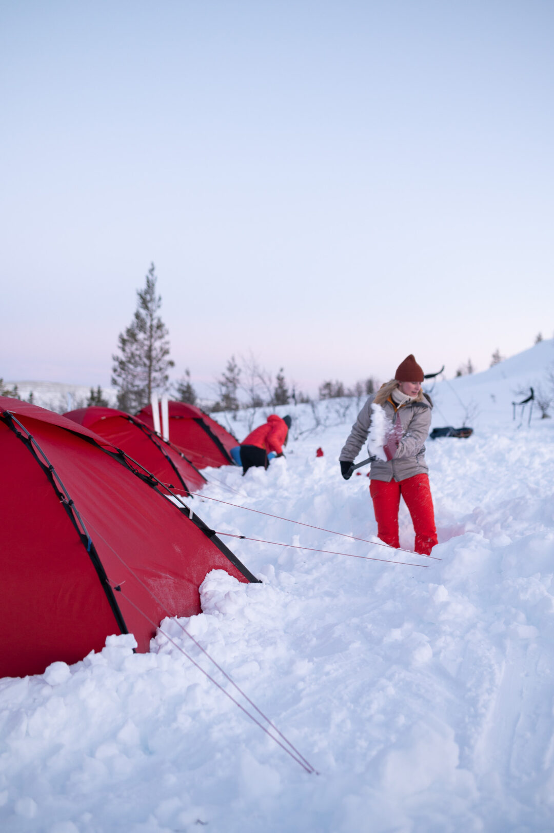Women with skis setting up red tent on a snow-covered winter camping trip in Sweden
