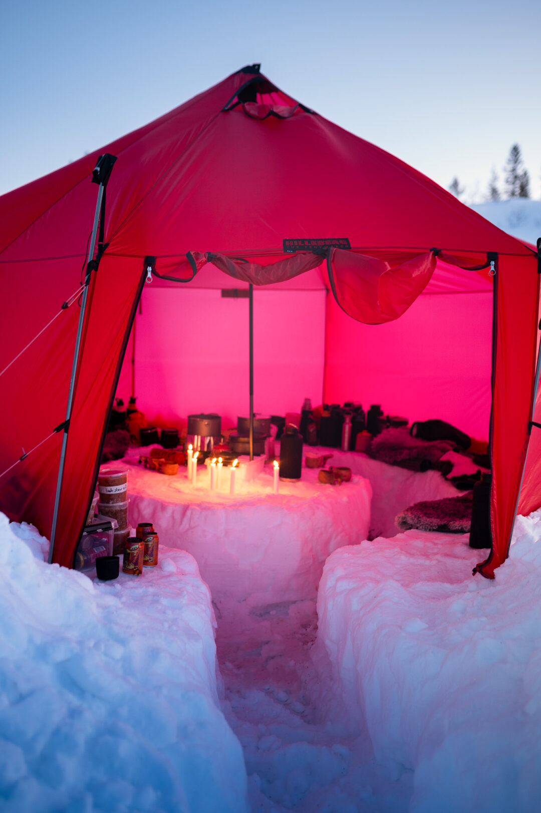 Red winter camping tent with candles on a snowy table in Sweden, backcountry ski camp setting