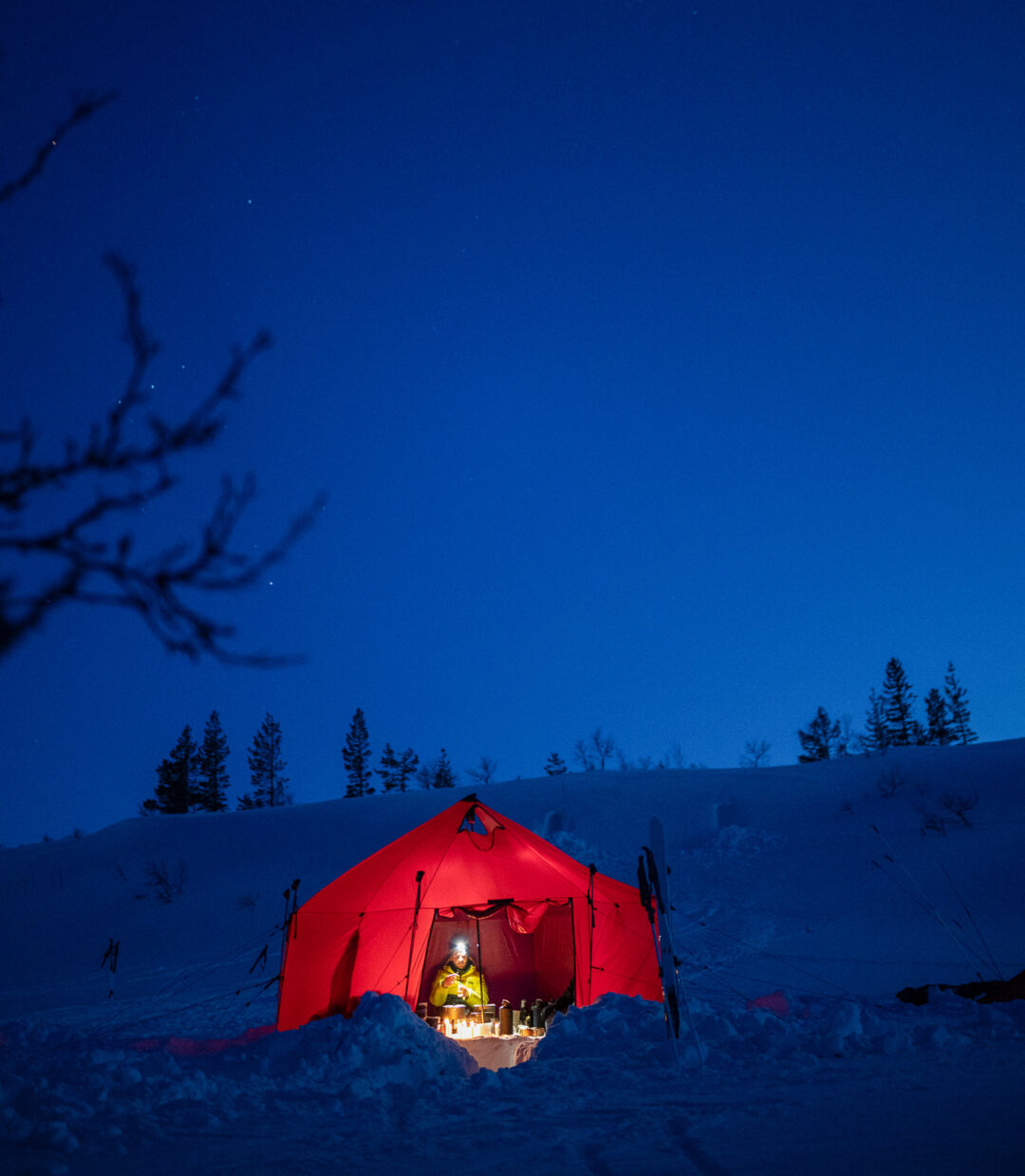 Lit winter camping tent inside a snowy hillside at night under a dark blue sky