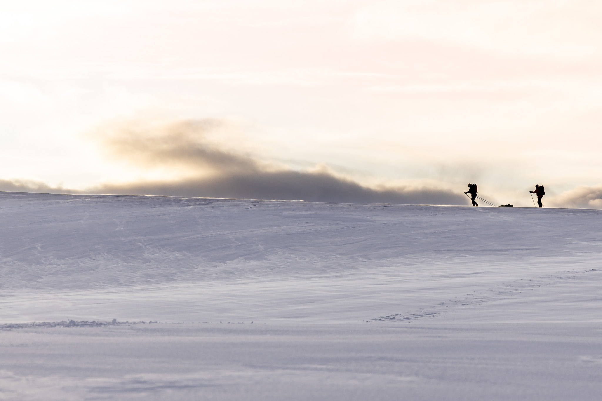 Two women backcountry skiers silhouette on a snowy slope at dusk, with ski poles in the landscape