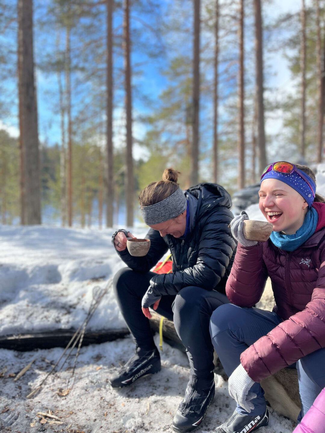 Women snowshoeing in a snowy forest, sitting in winter clothes and laughing with hot drinks