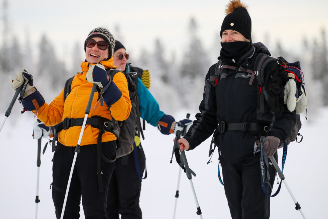 Women backcountry skiing in snowy Swedish forest, walking with poles and winter backpacks