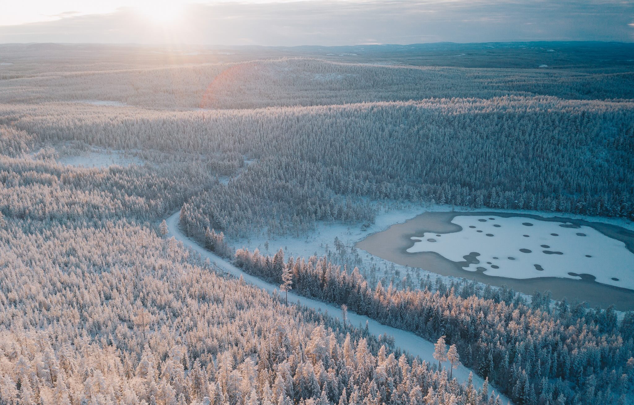 Aerial view of snowy forest with a frozen river and ice-covered lake in winter