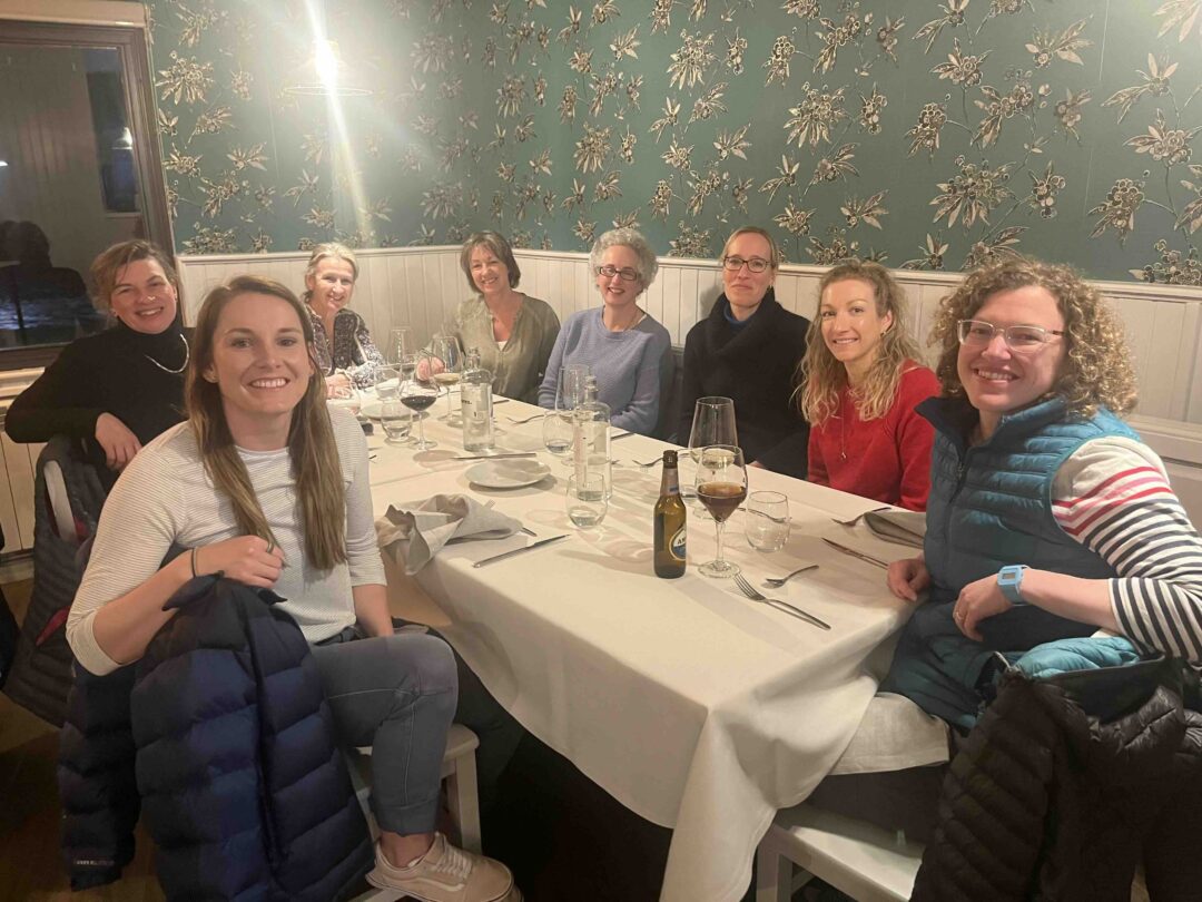 Group of friends smiling at a long dinner table in a cosy restaurant, enjoying wine and conversation