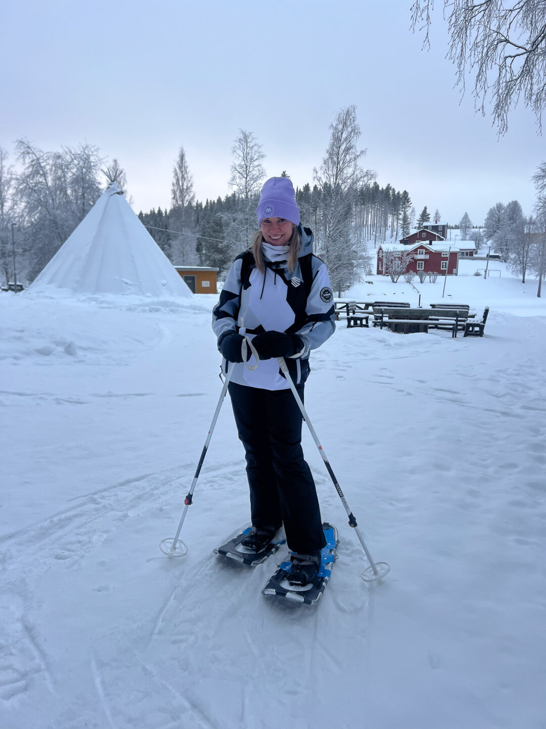 Skier in winter Lapland standing on cross-country skis near a snowy tipi and red cabins