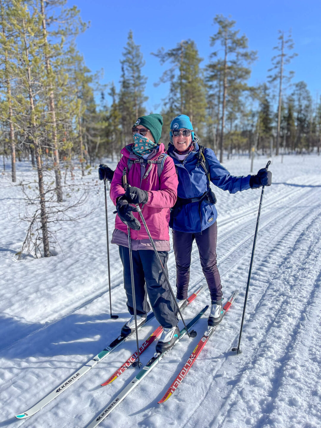 Two cross-country skiers in a snowy forest, smiling as they glide along fresh tracks