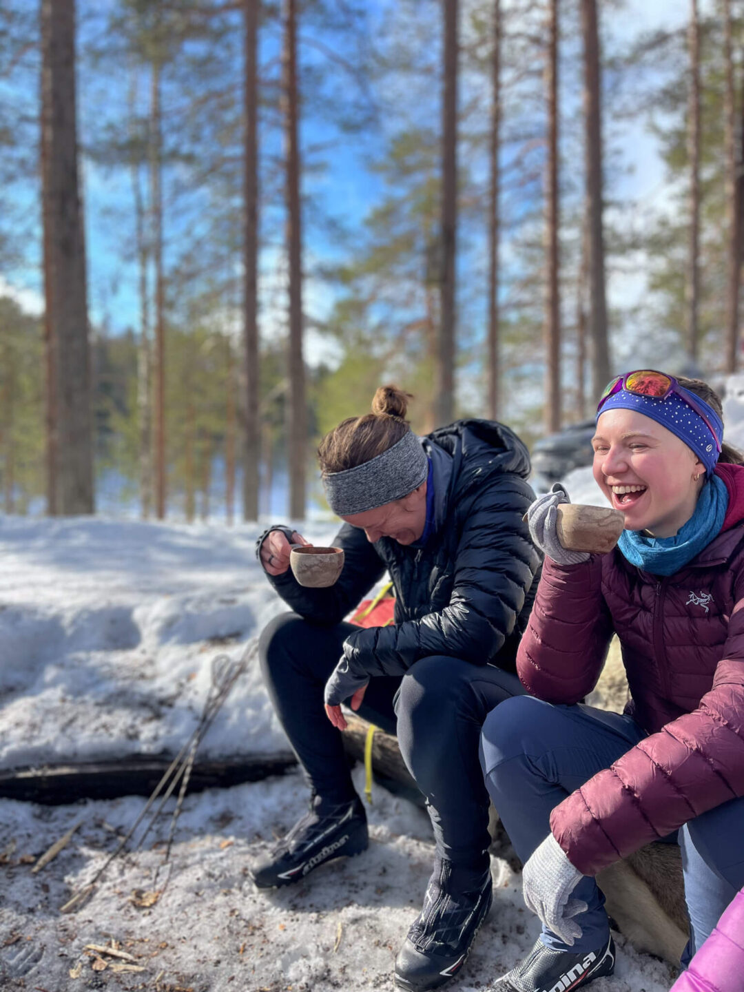 Friends enjoying a break during cross-country skiing in Finland, laughing in the snowy forest landscape