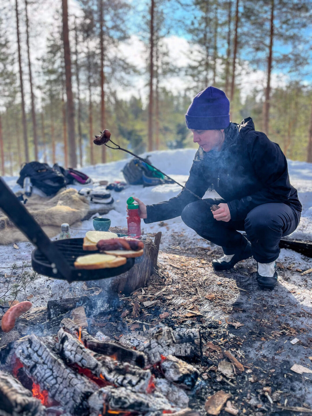 Cross-country ski tour camper in winter clothing cooking by a campfire in a snowy pine forest