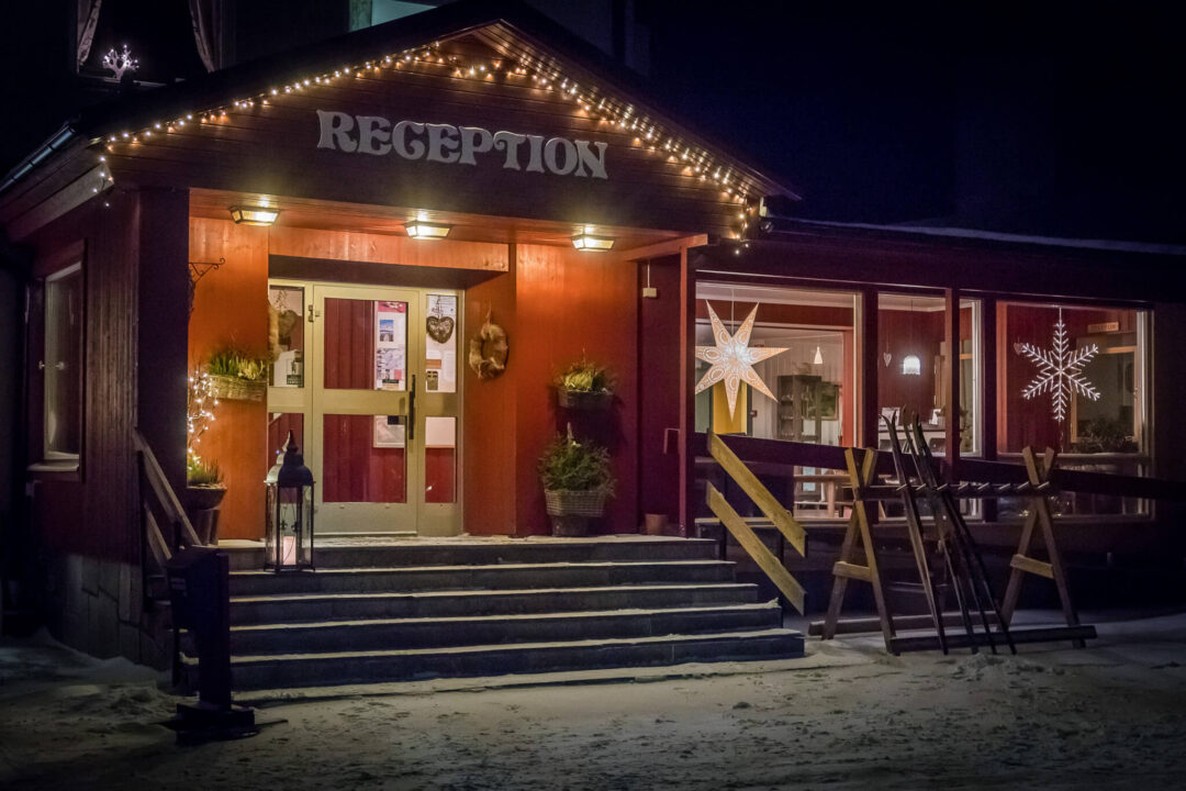 Well-lit reception building entrance at night in Sweden, with “RECEPTION” sign and outdoor wooden chairs