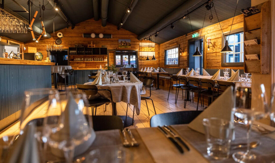 Cozy Swedish lodge dining room with set tables, warm lighting and wooden bar area in the background