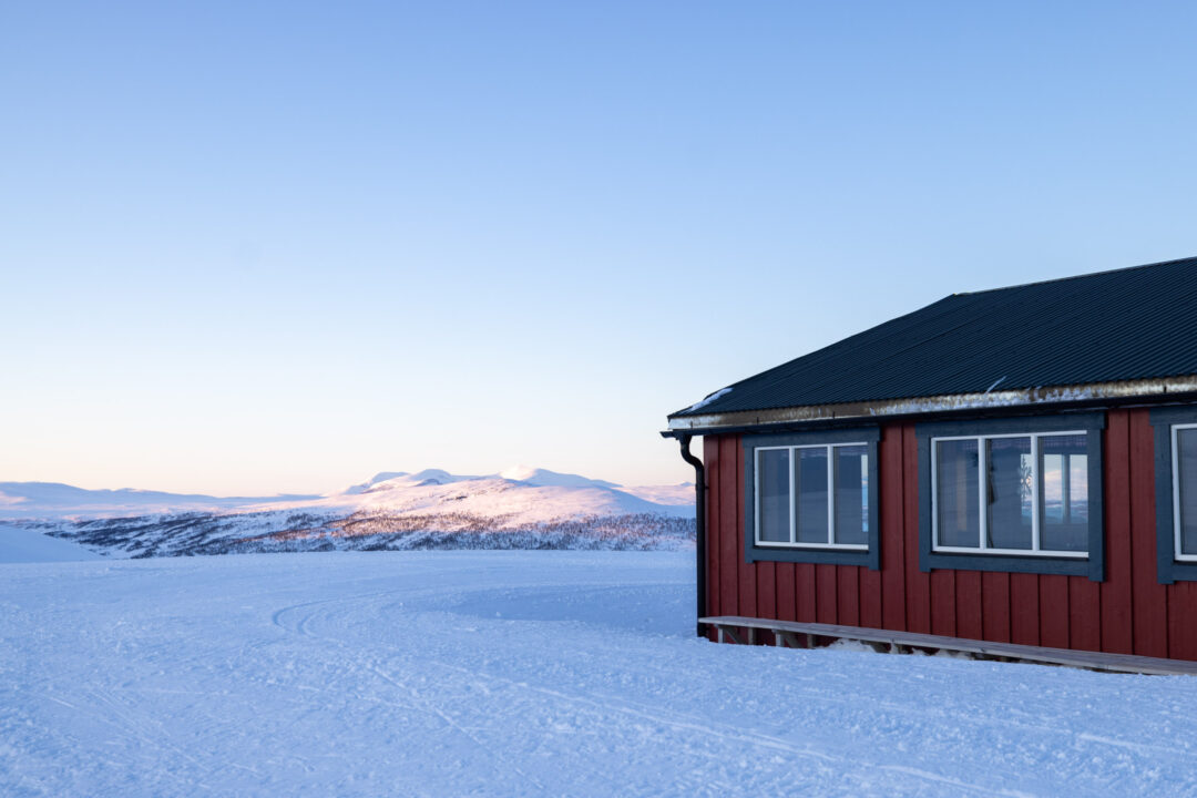 Snowy landscape with a red cabin and ski tracks in Sweden at dusk