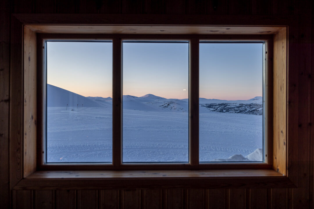 Snowy mountain landscape with ski tracks seen through a wooden cabin window at dusk