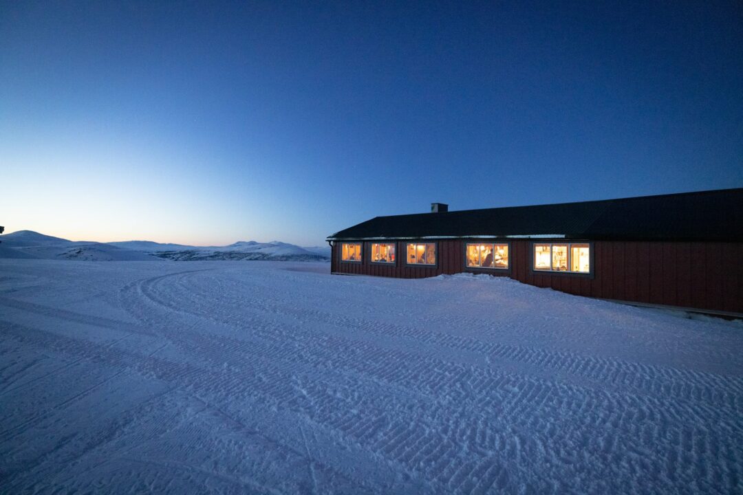 Snow-covered ski lodge cabin at dusk with warm windows, on a snowy landscape