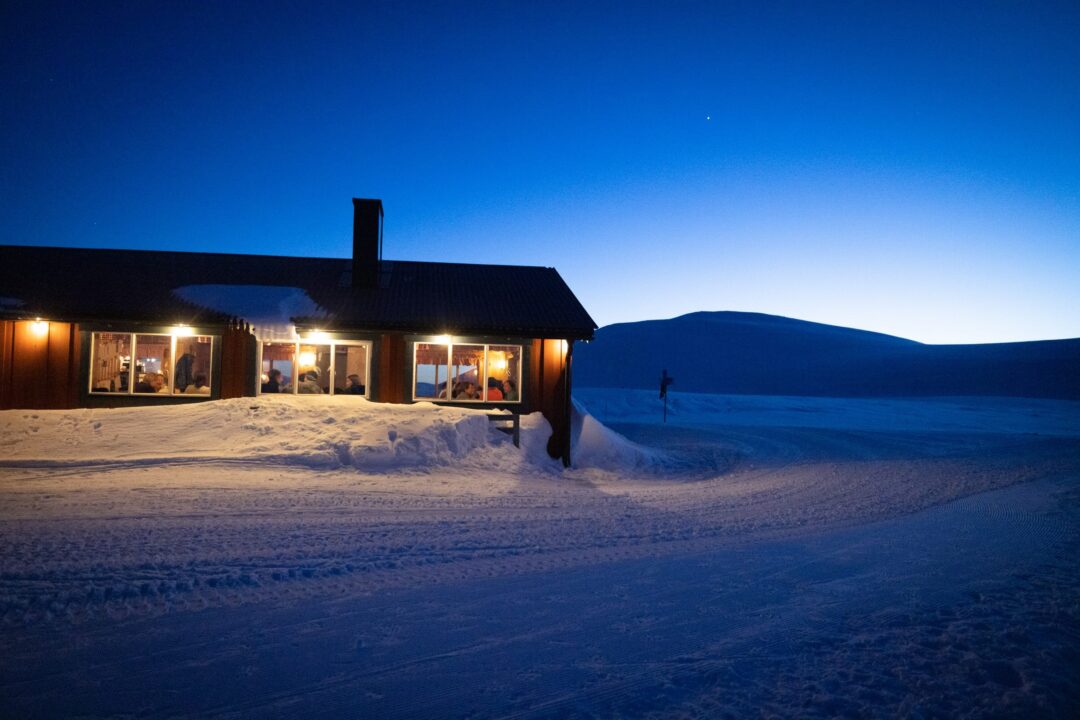 Snowy wooden lodge at dusk with lit windows in a winter landscape