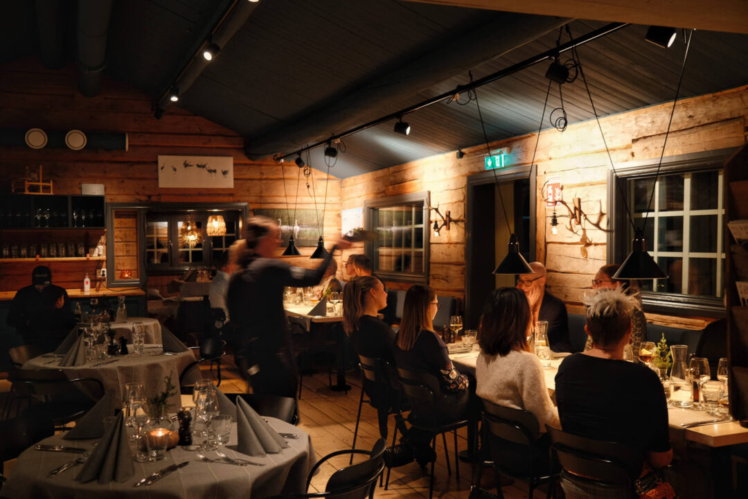 Cozy Swedish log-cabin dinner with candles and guests seated at tables in warm evening light