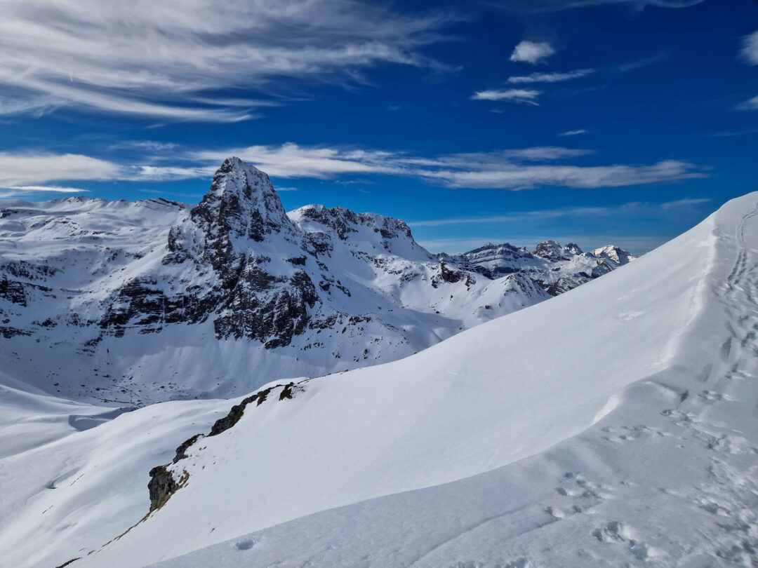 Snowshoeing on a snowy mountain ridge with tracks and views of Pyrenees peaks under blue sky