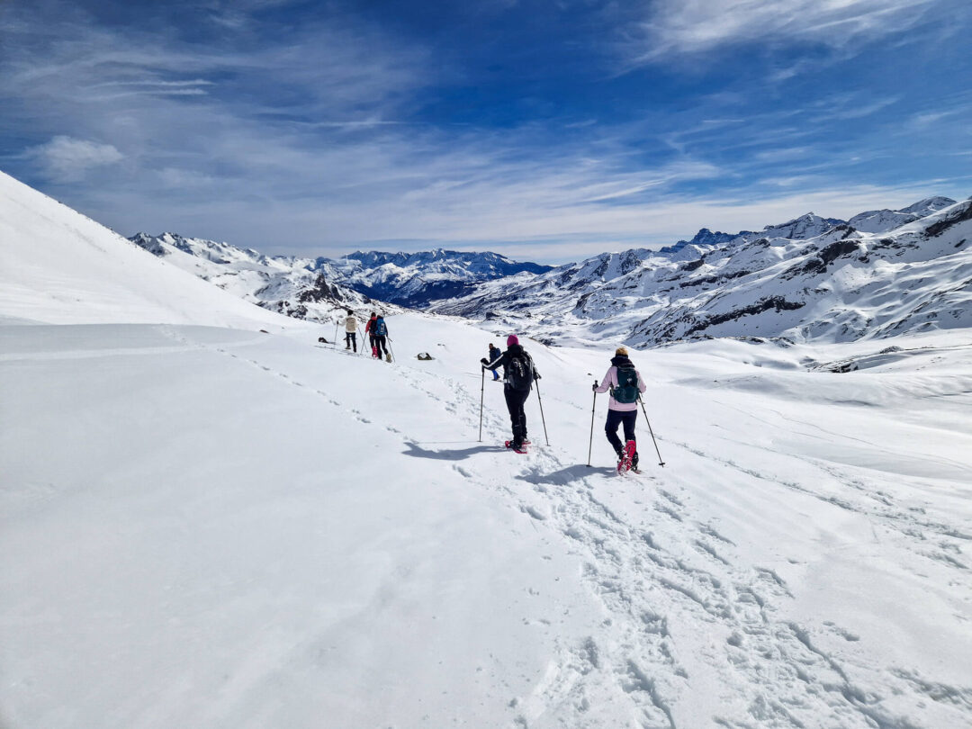Snowshoers trek through snowy Pyrenees mountains on a winter hiking trail under a clear blue sky