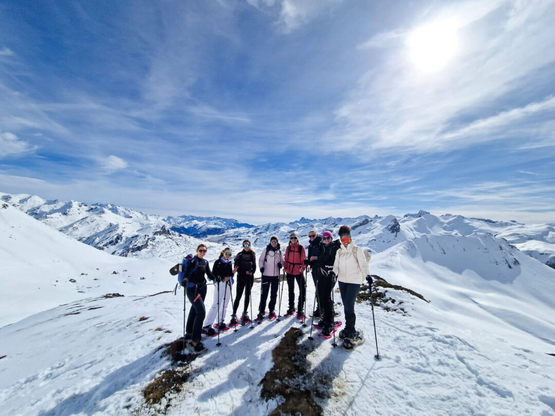 Group snowshoeing on a snowy mountain ridge in the Pyrenees under a bright winter sky.
