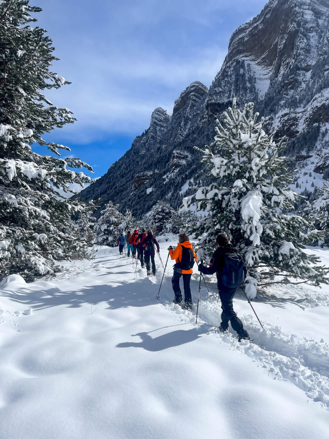 Snowshoe hikers trekking through snowy Pyrenees mountain valley beneath towering rock cliffs