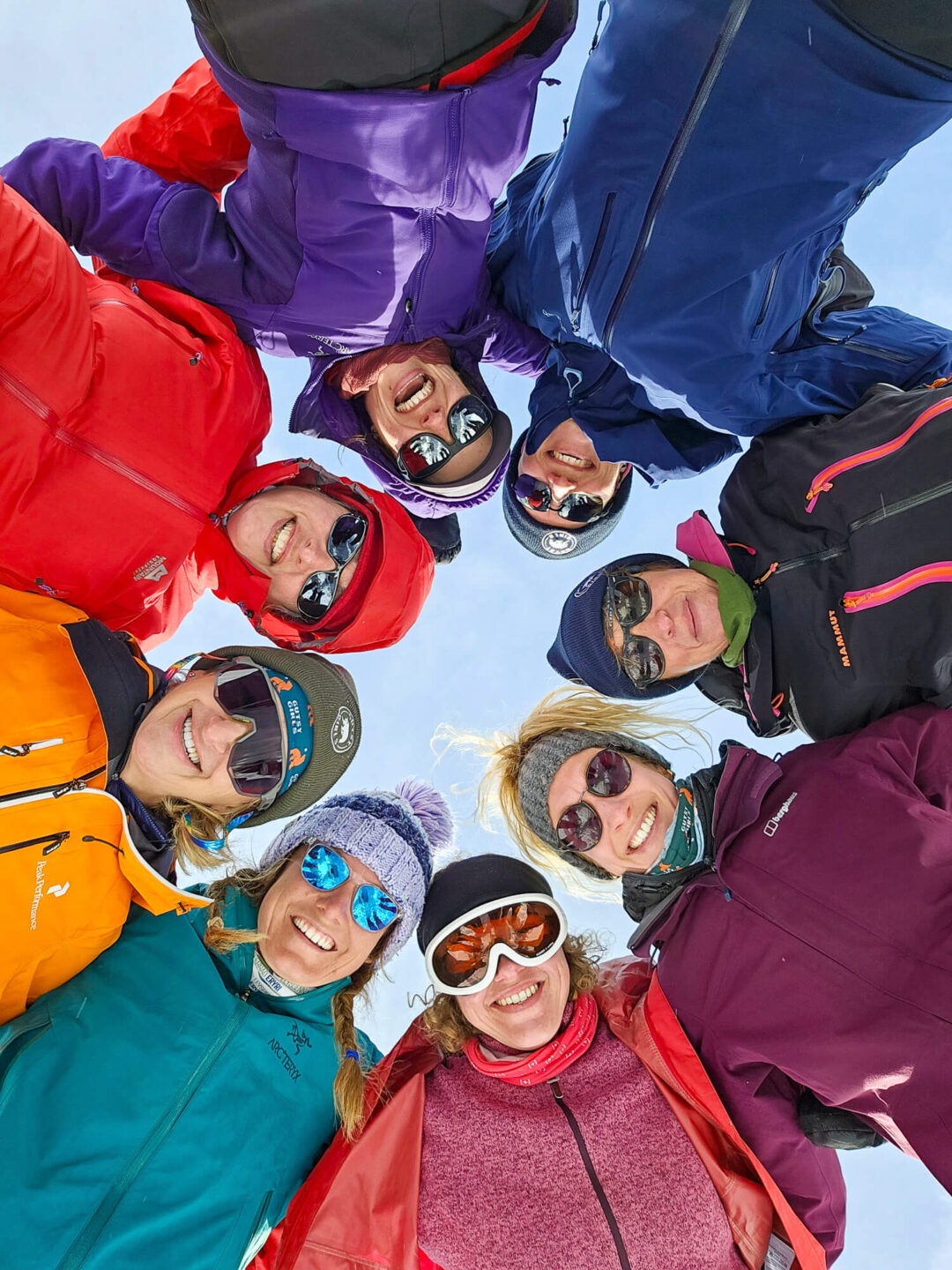 Group of winter hikers in colourful jackets and goggles smiling against the snowy sky on a snowshoe trek
