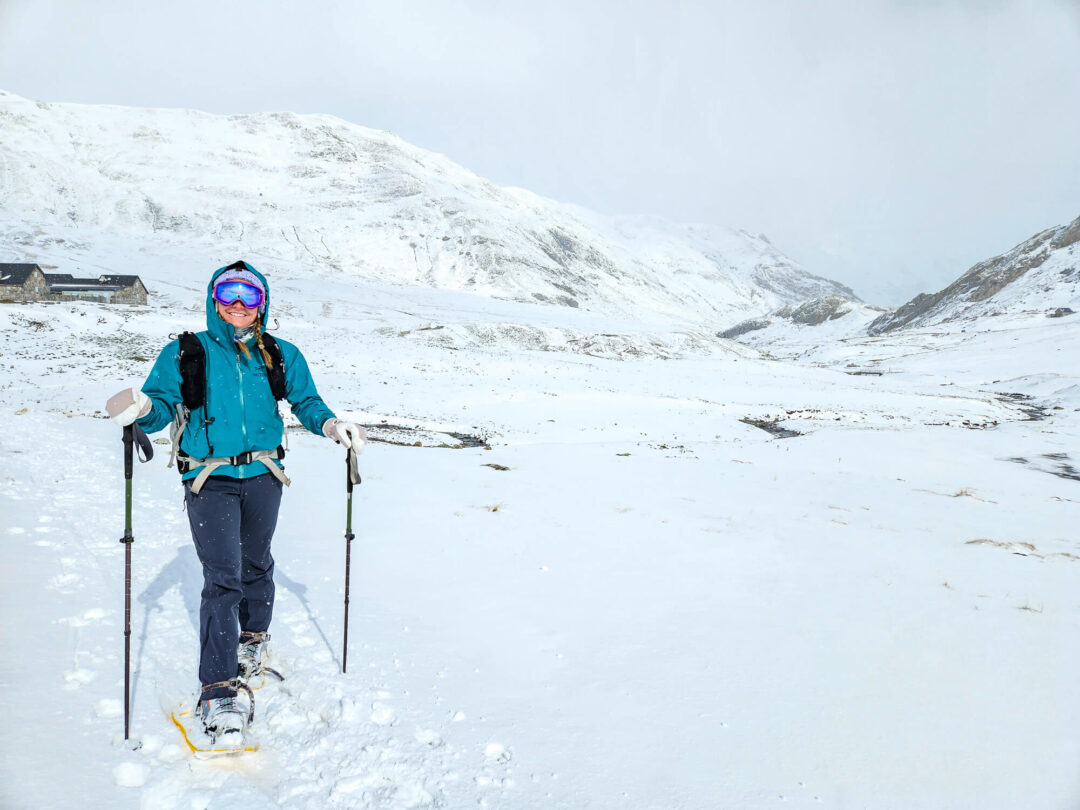 Snowshoer in blue jacket trekking through snowy Pyrenees valley, with mountain peaks in winter.