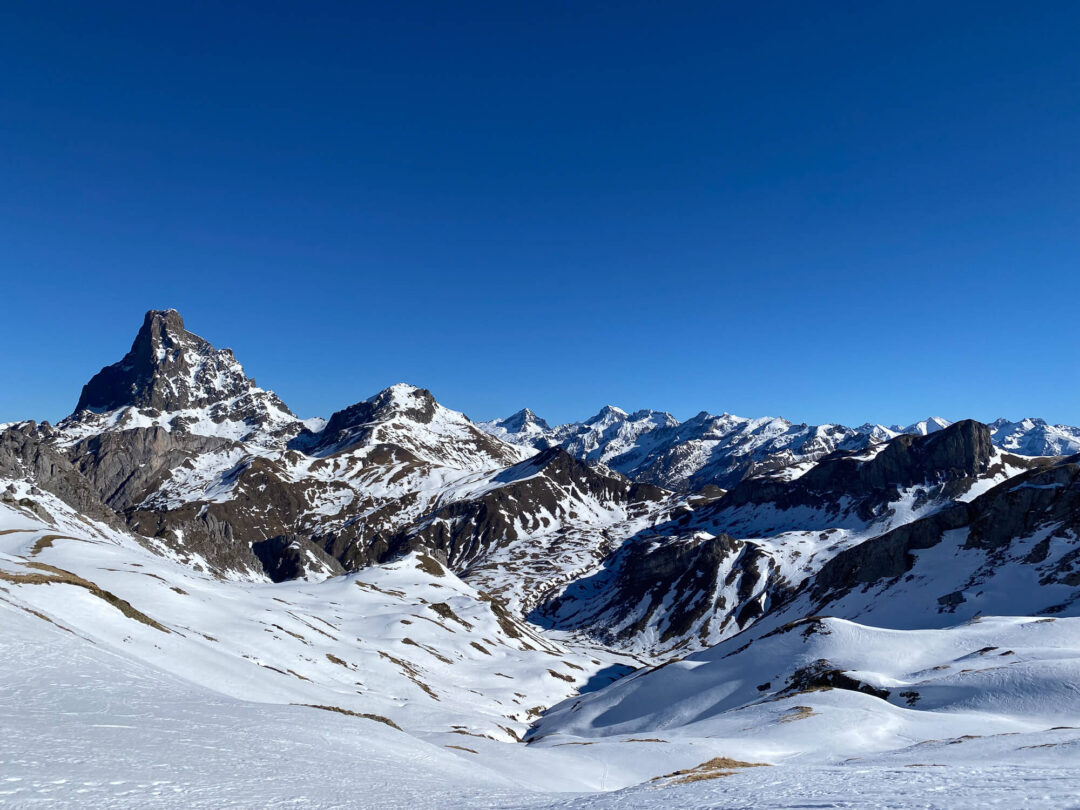 Snowy Pyrenees mountain peaks and valleys with winter tracks under a clear blue sky, ideal for snowshoeing and hiking