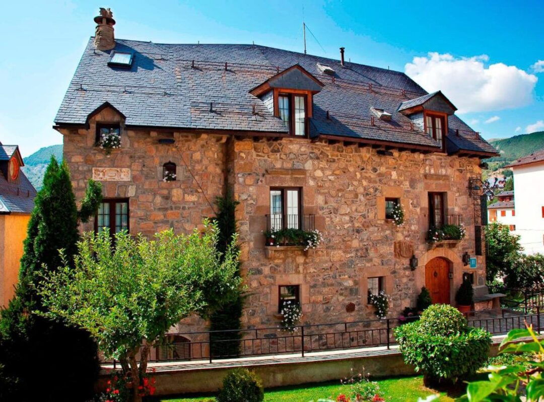 Rustic stone house with slate roof and mountain backdrop, in a European alpine village