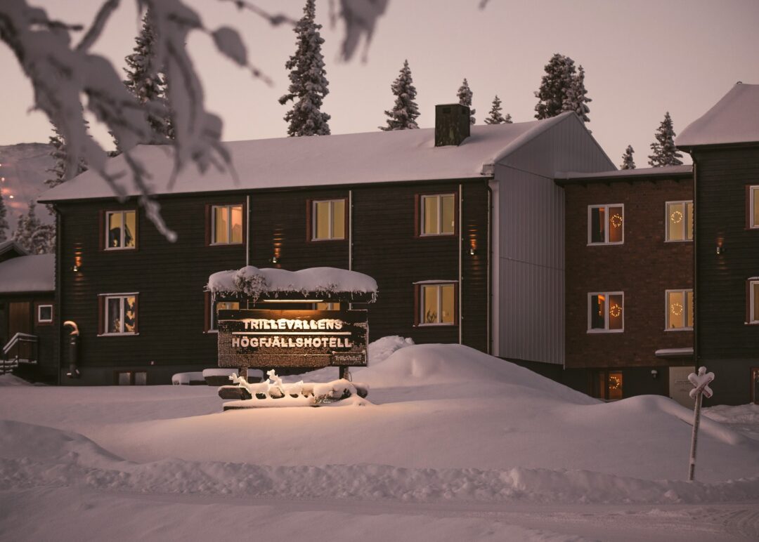 Snow-covered ski lodge with lit windows at dusk, viewed from snowy grounds