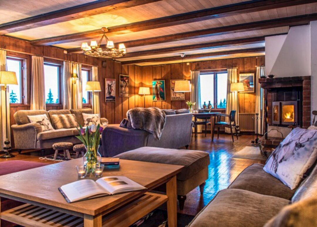 Cozy cabin living room with fireplace, sofas, and dining table by large windows