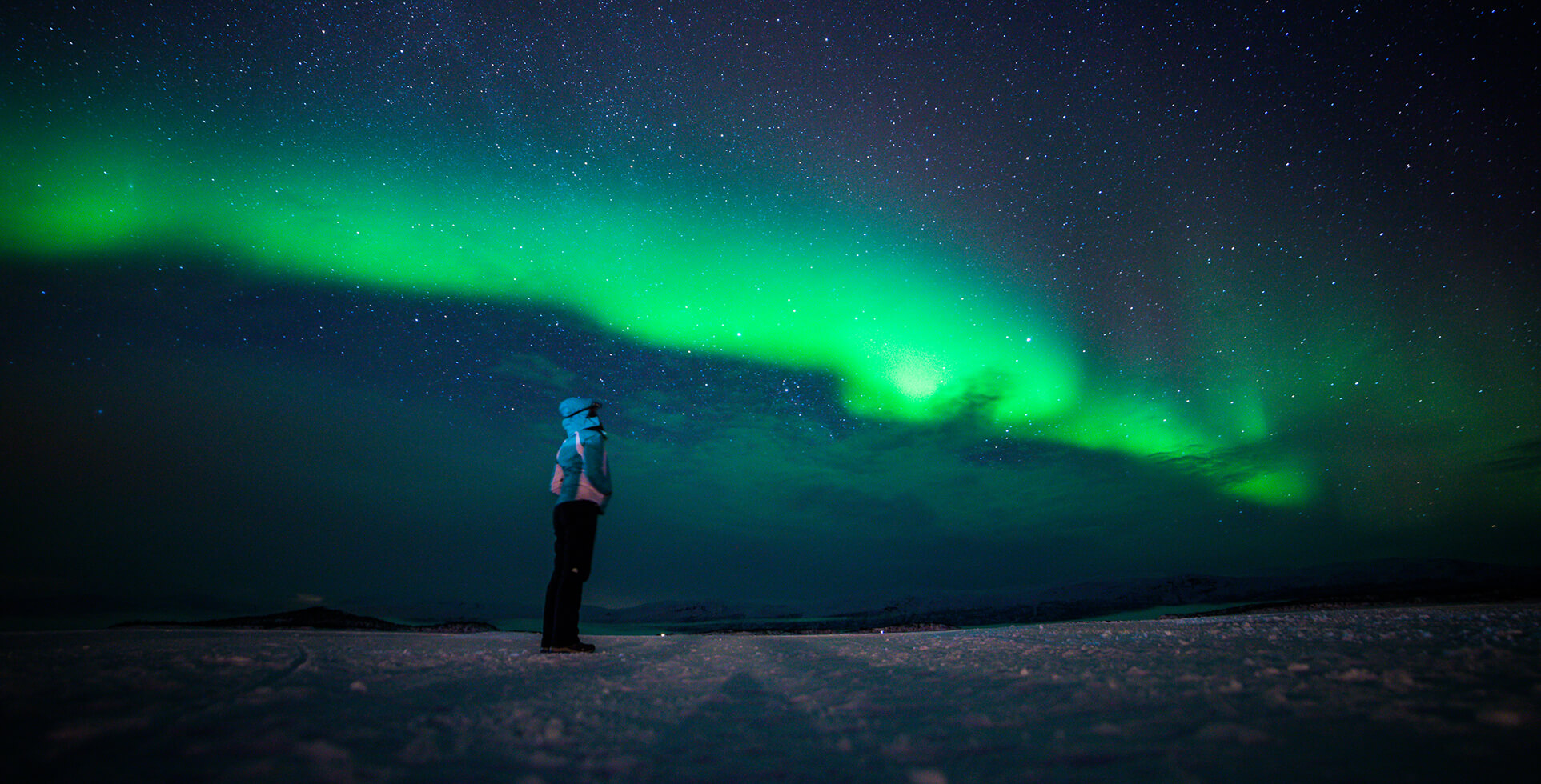 Woman standing on snowy ground under the northern lights in a dark winter sky