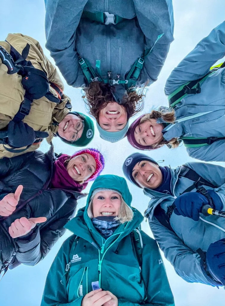 Smiling group snowshoeing in snowy Finland, bundled in winter jackets and helmets, looking up at the camera