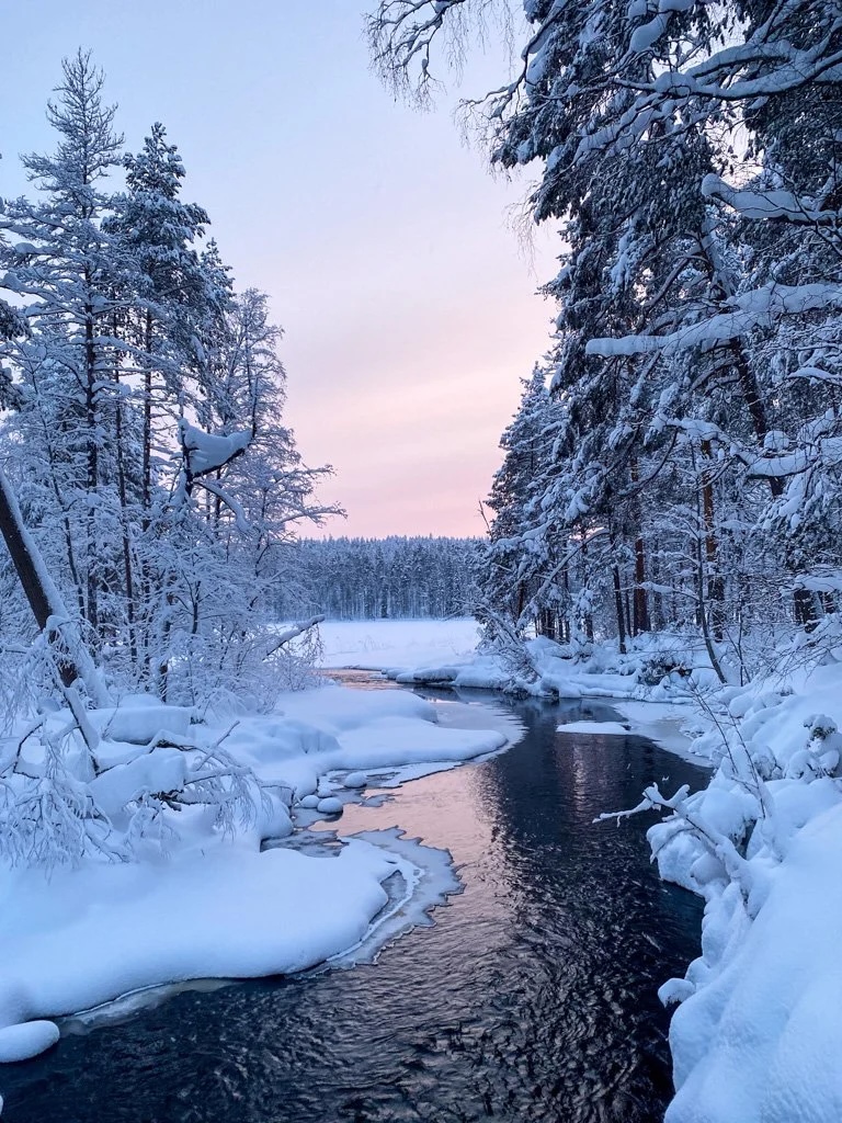 Snowy Finnish forest river at dusk, with snow-covered trees and tracks ideal for snowshoeing adventures