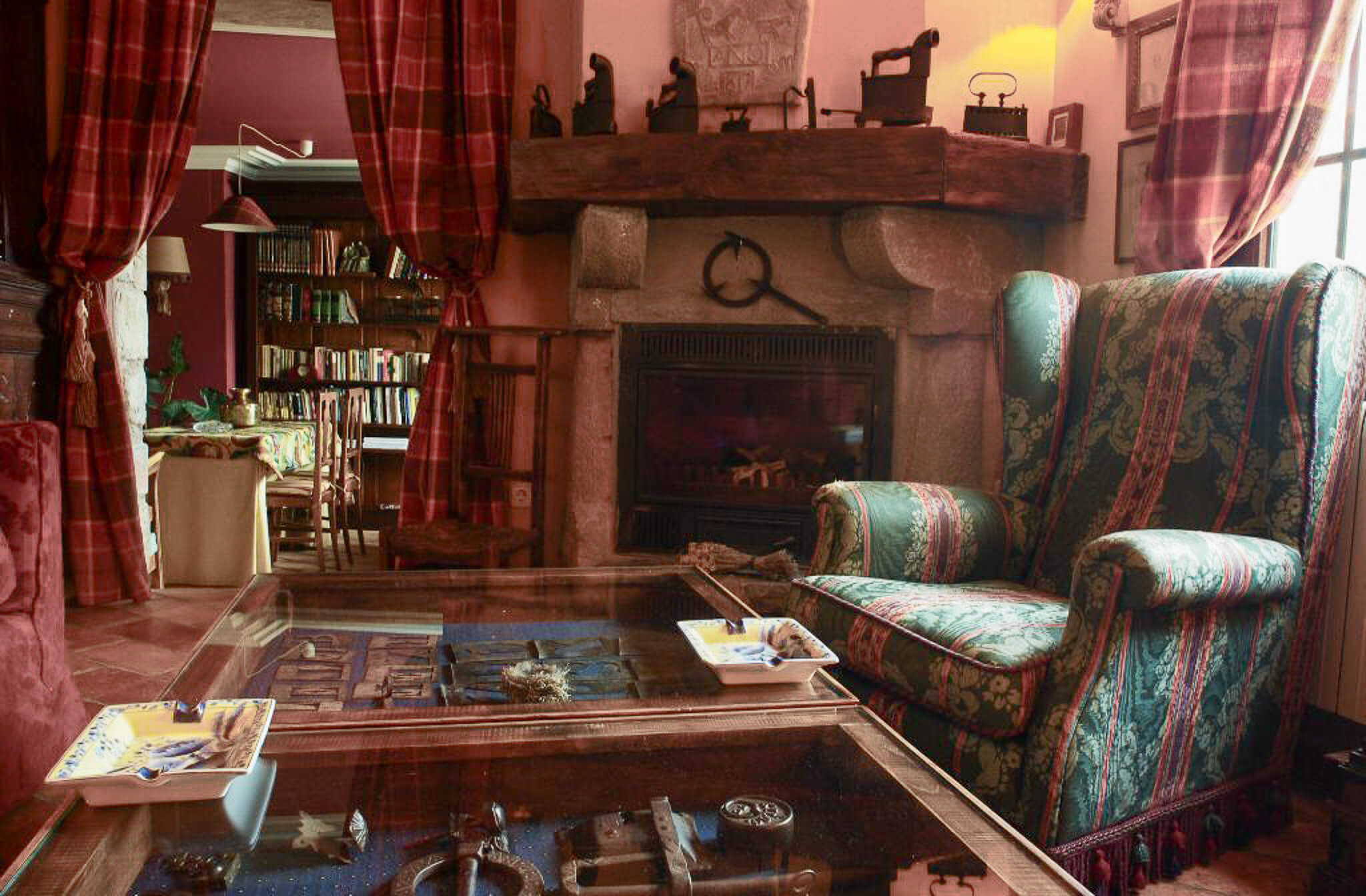 Cosy Pyrenees lodge living room with stone fireplace, patterned armchairs and winter travel maps on a table