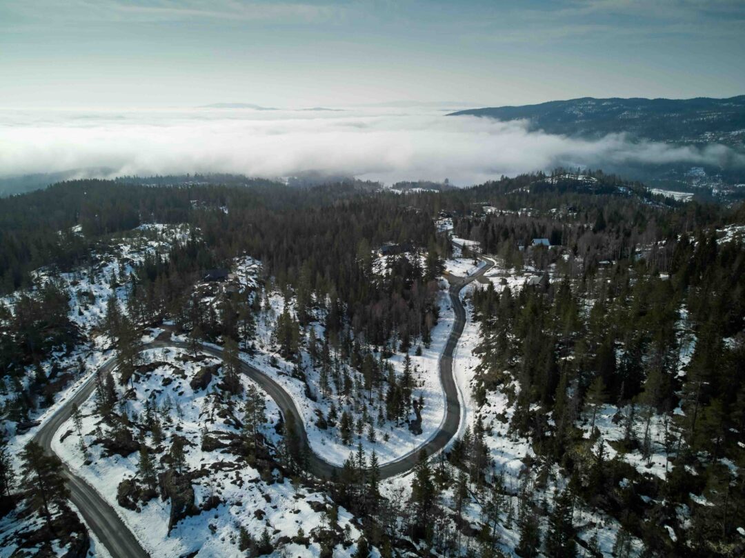 Winding road through snowy forest valley viewed from above under low cloud and winter haze.