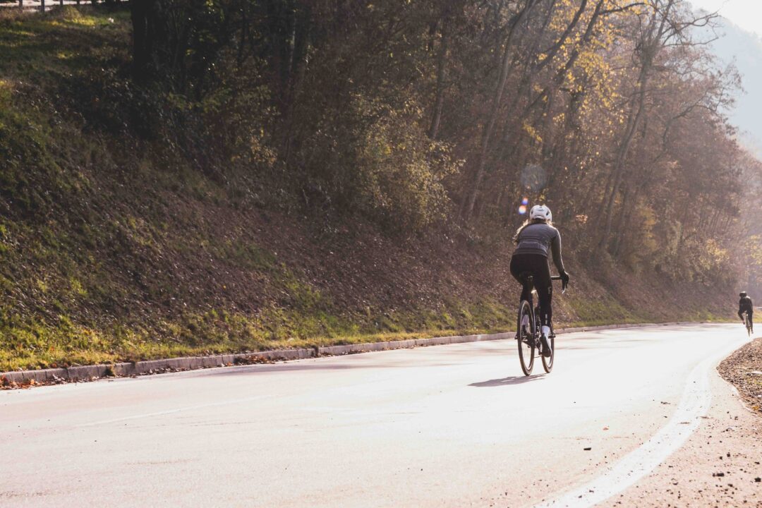 Woman cycling on a quiet road through autumn woods, wearing a helmet and riding a road bike