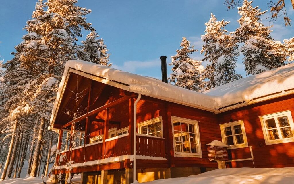 Warm wooden cabin in snowy Finland surrounded by frosted pine trees under winter sunshine