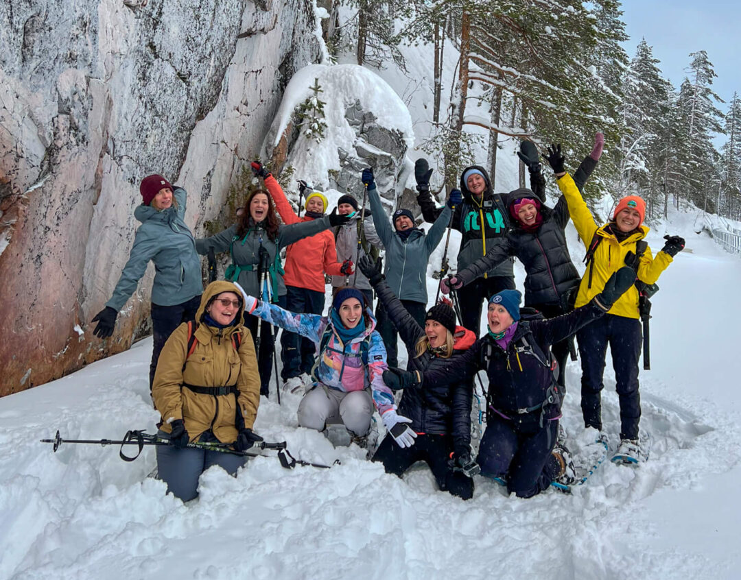 Group of winter snowshoeing adventurers posing in Finland’s snowy pine forest near a rock face