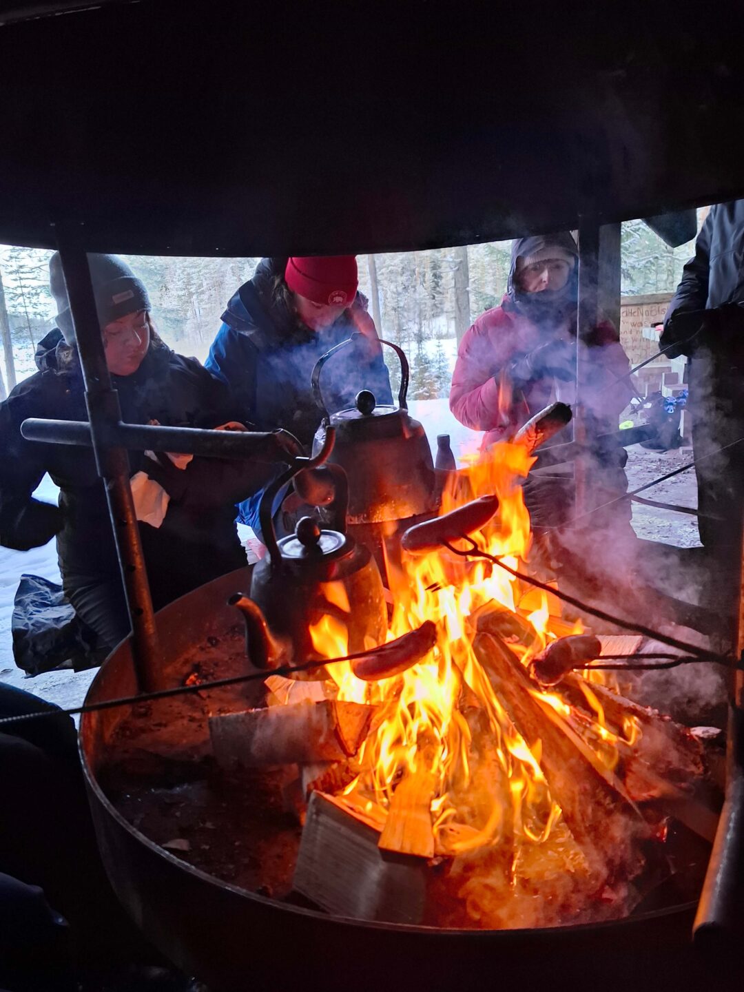 Women warm up and boil water over an open fire during a snowshoeing outing in Finland
