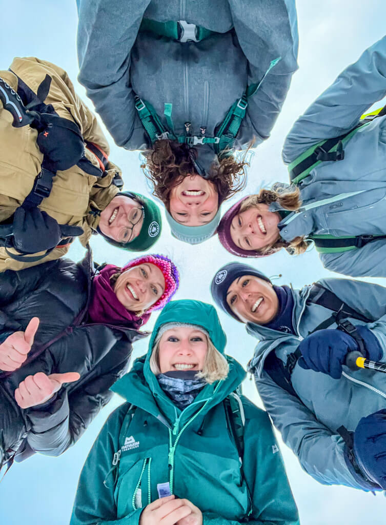 Group of friends cheering in winter coats during a snowshoe adventure in Finland under snowy sky