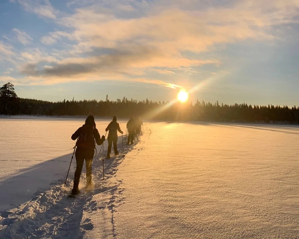 Dog sledding in Lapland: two mushers walk beside the sled on a frozen lake at sunrise