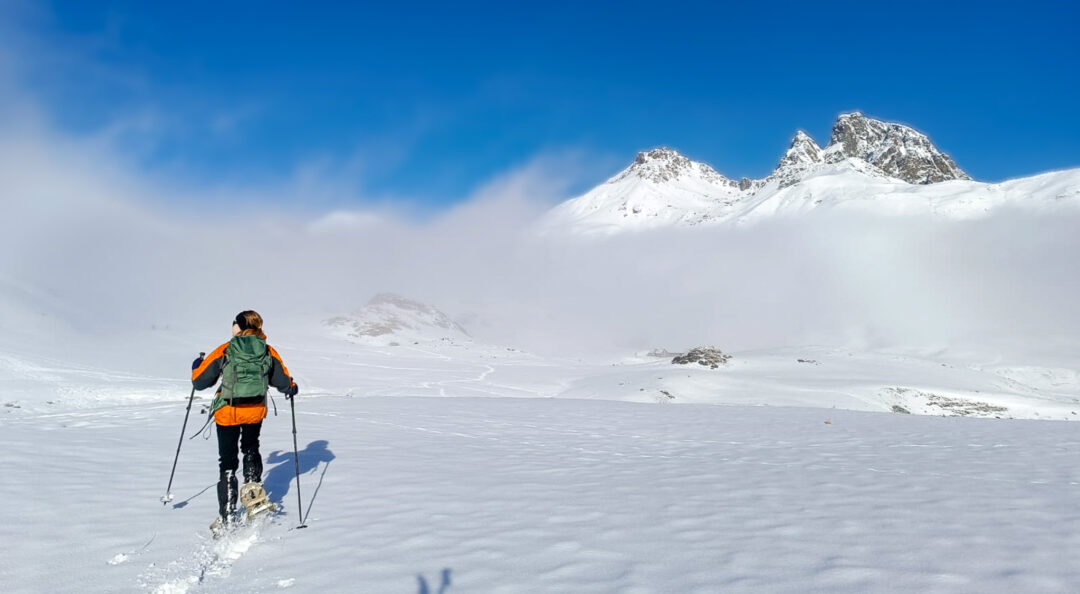 Woman snowshoeing on a snowy mountain ridge under a clear blue sky in winter conditions